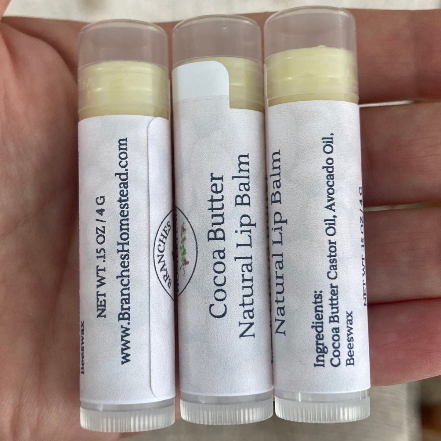 Hand holding four lip balm tubes with visible labels.