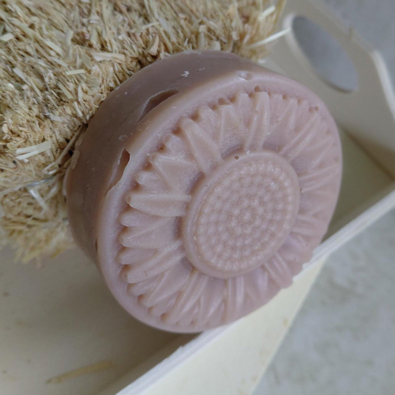 Pink soap bar with textured design on a beige scrubber