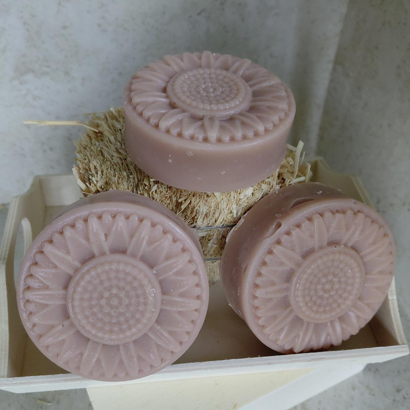 Three pink soaps with textured surfaces in a white container on a light gray surface.