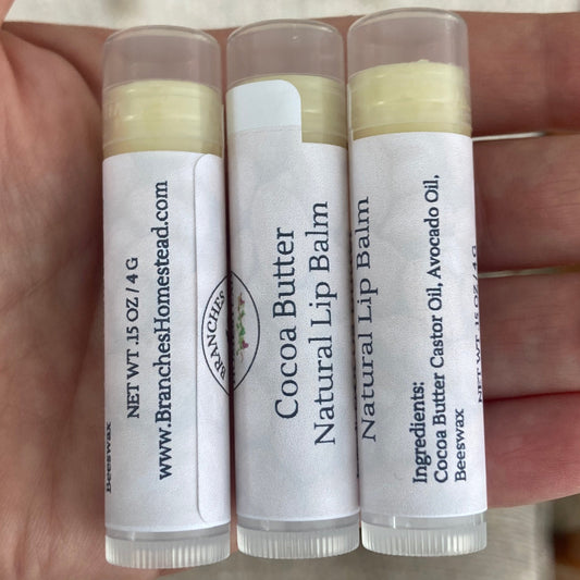 Hand holding four lip balm tubes with visible labels.