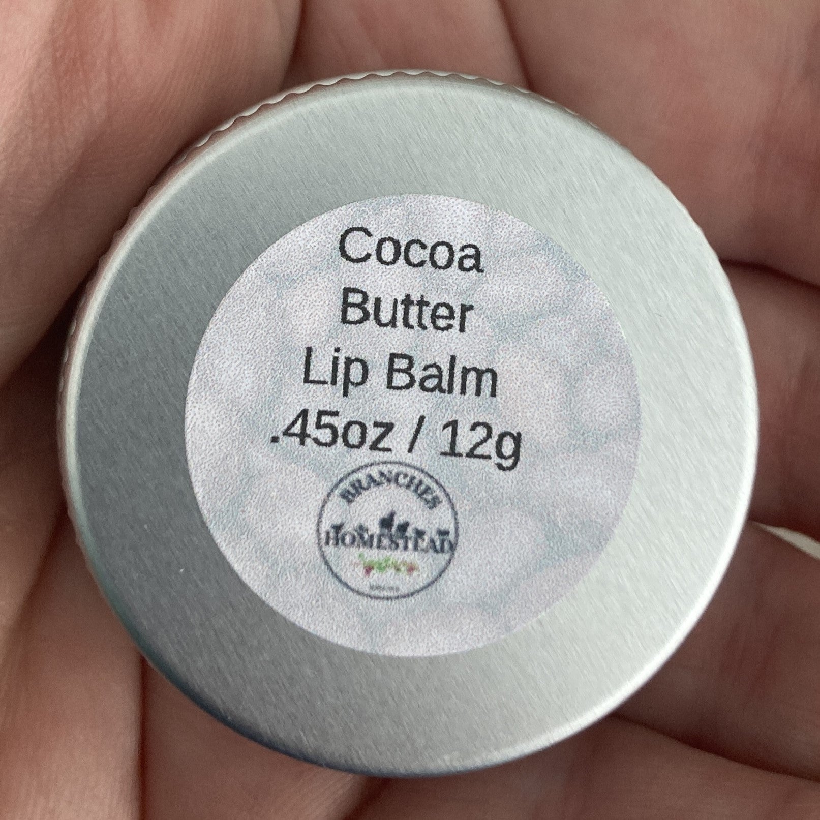 Cocoa Butter Lip Balm container with label held in hand