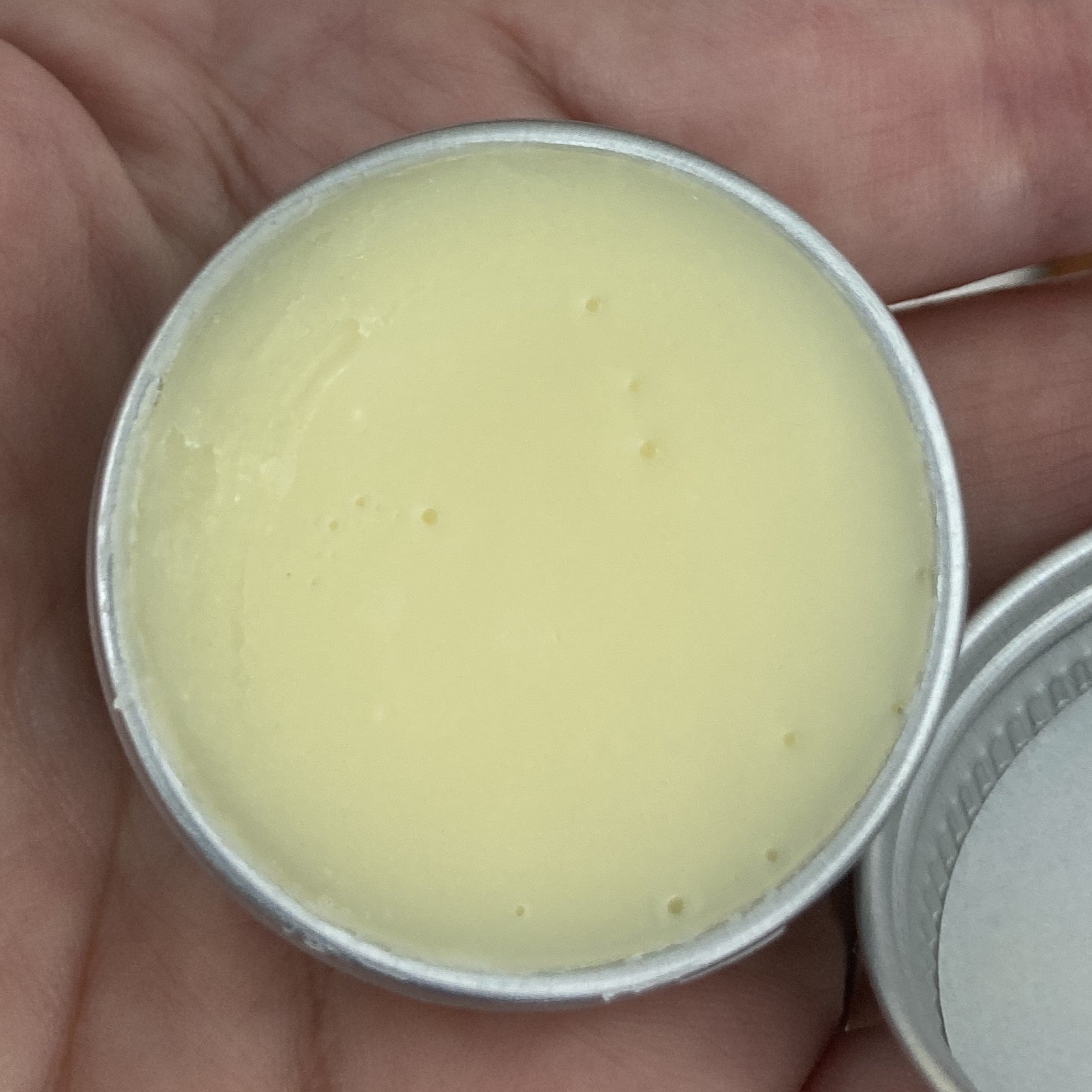 Cream color Balm in a metal container held between fingers
