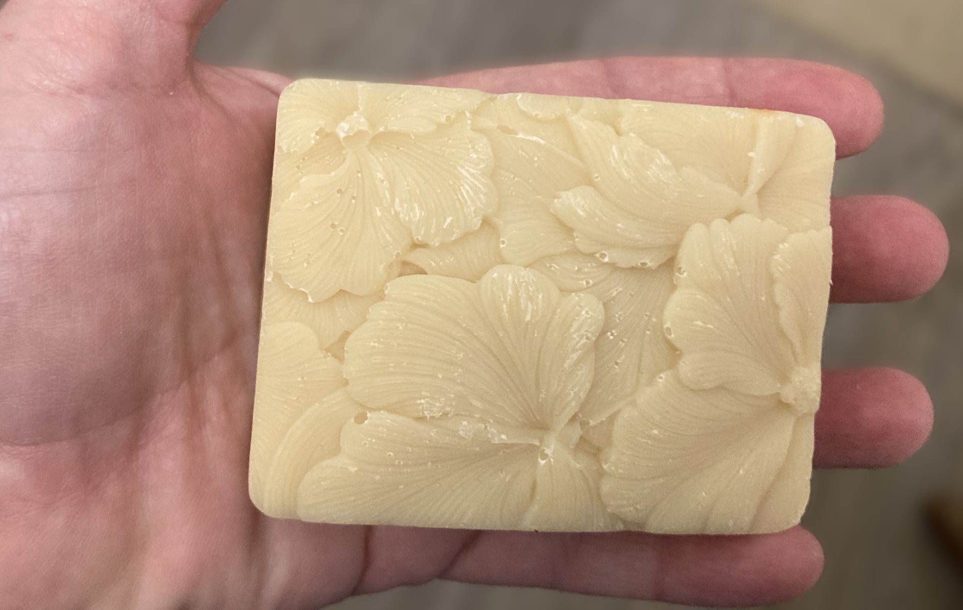 Hand holding a bar of cream color soap with floral design